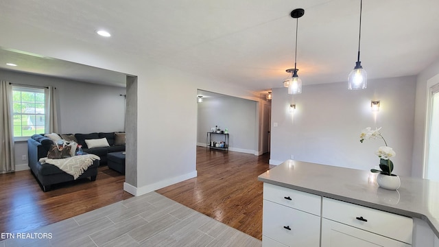 kitchen with white cabinets, open floor plan, baseboards, wood finished floors, and pendant lighting