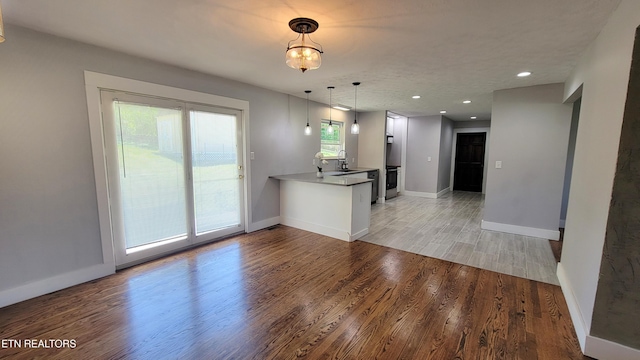 kitchen featuring a peninsula, light wood-type flooring, white cabinets, a sink, and decorative light fixtures
