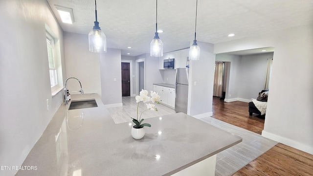 kitchen with white cabinets, appliances with stainless steel finishes, a sink, baseboards, and light wood-type flooring