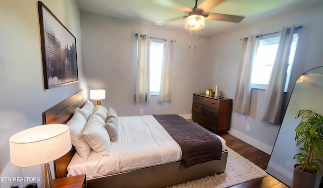 bedroom featuring a ceiling fan, baseboards, multiple windows, and wood finished floors