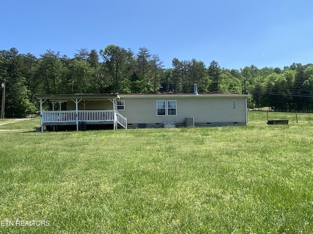 back of property with central air condition unit, crawl space, and a view of trees