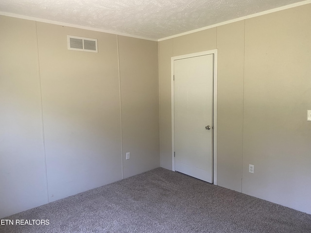spare room with a textured ceiling, carpet flooring, visible vents, ornamental molding, and a decorative wall