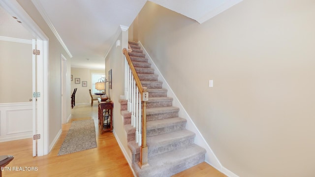 stairs with ornamental molding and wood finished floors