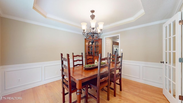 dining area featuring an inviting chandelier, a tray ceiling, and light wood-style flooring