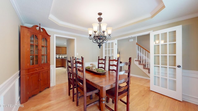 dining space with crown molding, an inviting chandelier, light wood-style floors, french doors, and a tray ceiling