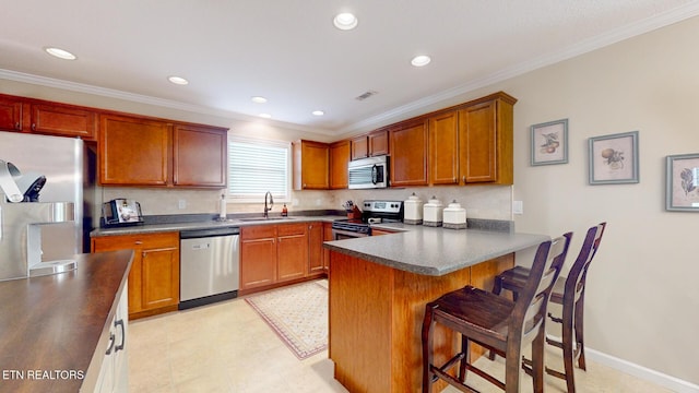 kitchen with a peninsula, dark countertops, a kitchen breakfast bar, a sink, and appliances with stainless steel finishes