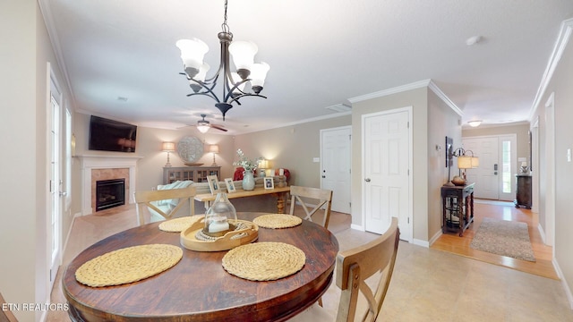 dining area featuring baseboards, ornamental molding, ceiling fan with notable chandelier, and a tile fireplace