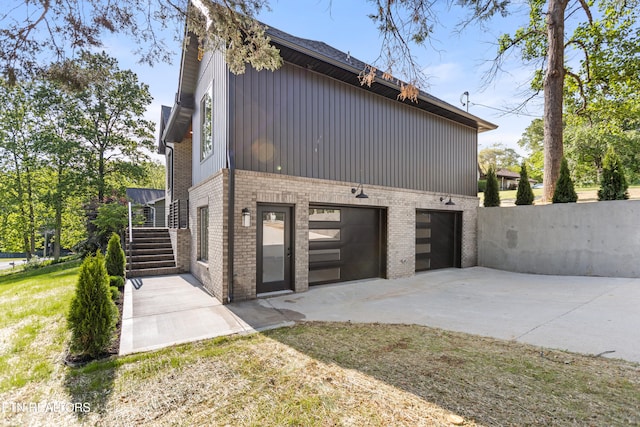 view of side of property featuring concrete driveway, brick siding, an attached garage, and board and batten siding