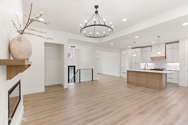 unfurnished living room with baseboards, recessed lighting, a chandelier, a sink, and light wood-style flooring