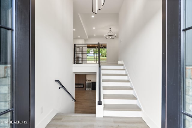 stairway with baseboards, recessed lighting, wood finished floors, and a notable chandelier