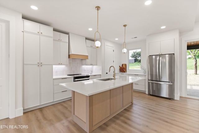 kitchen with a sink, light countertops, premium range hood, freestanding refrigerator, and decorative backsplash