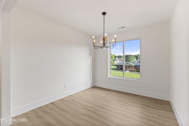 spare room with baseboards, light wood-type flooring, a chandelier, and visible vents