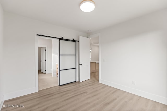 unfurnished bedroom with baseboards, light wood finished floors, and a barn door