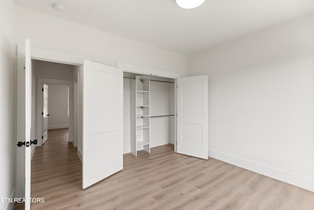 unfurnished bedroom with baseboards, light wood-style flooring, and a closet