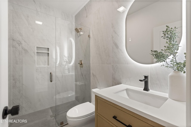 bathroom with vanity, a marble finish shower, toilet, and tile walls