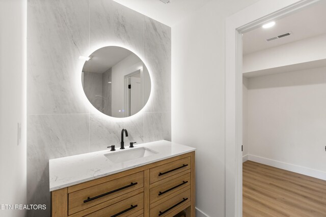 bathroom with visible vents, vanity, wood finished floors, baseboards, and backsplash