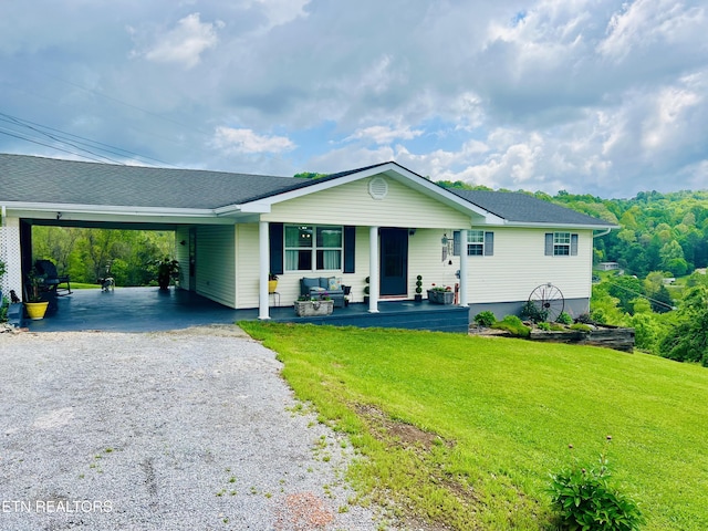 ranch-style home with a porch, a front lawn, a shingled roof, an attached carport, and gravel driveway