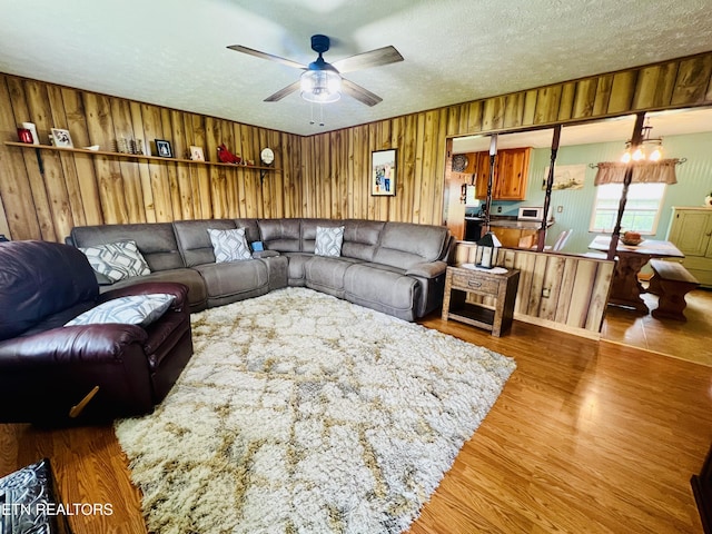 living room with a ceiling fan, wood walls, wood finished floors, and a textured ceiling