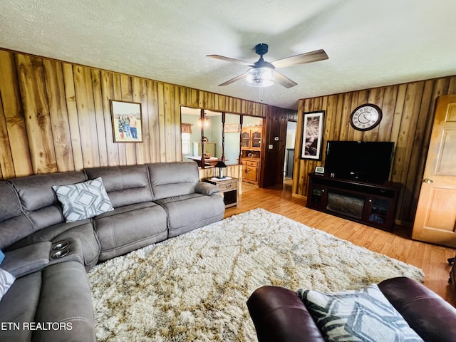 living area with wood finished floors, wooden walls, a ceiling fan, and a textured ceiling