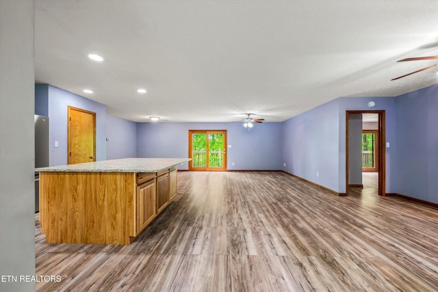 kitchen featuring wood finished floors, a kitchen island, baseboards, brown cabinets, and a ceiling fan