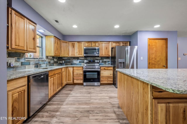 kitchen featuring light stone counters, a sink, stainless steel appliances, light wood-type flooring, and visible vents