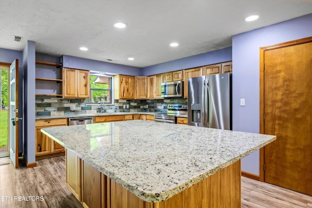 kitchen with light wood-style flooring, appliances with stainless steel finishes, and tasteful backsplash