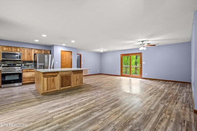 kitchen featuring appliances with stainless steel finishes, a ceiling fan, baseboards, wood finished floors, and a kitchen island