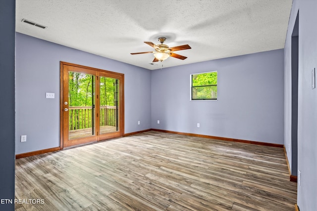 unfurnished room with visible vents, plenty of natural light, wood finished floors, and ceiling fan