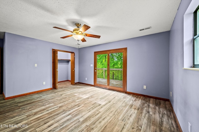 empty room with visible vents, wood finished floors, baseboards, ceiling fan, and a textured ceiling