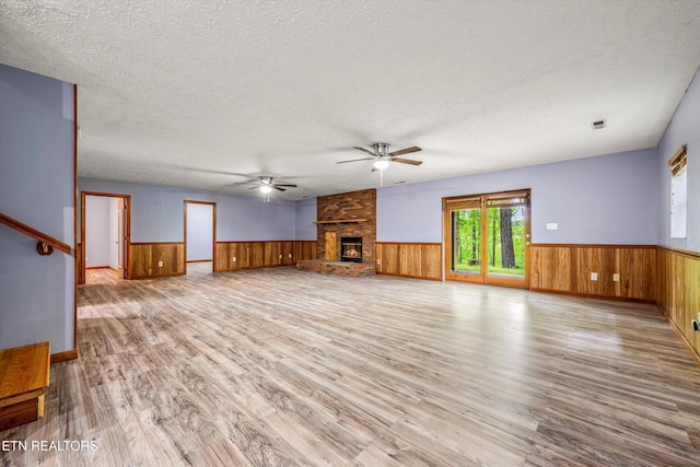unfurnished living room with a fireplace, ceiling fan, wood finished floors, and a wainscoted wall