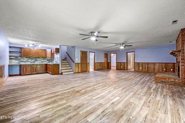 unfurnished living room with light wood-type flooring, a textured ceiling, ceiling fan, and wainscoting