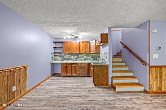 kitchen with a sink, light wood-style floors, light countertops, brown cabinetry, and backsplash