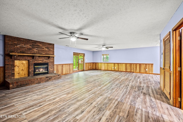 unfurnished living room with a textured ceiling, ceiling fan, wood finished floors, and a wainscoted wall
