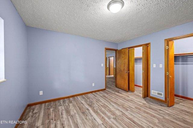 unfurnished bedroom featuring baseboards, a textured ceiling, wood finished floors, and visible vents