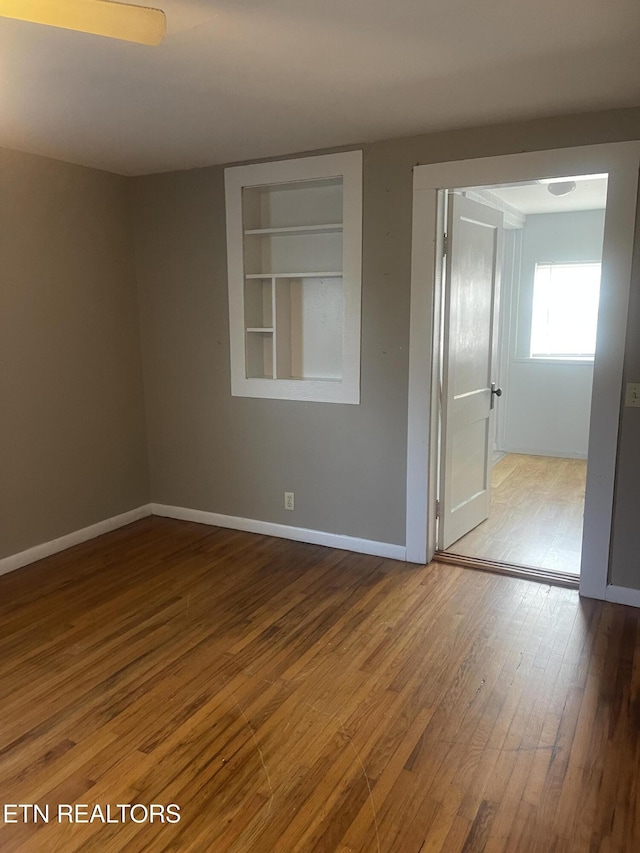 unfurnished room featuring baseboards, wood-type flooring, and built in shelves