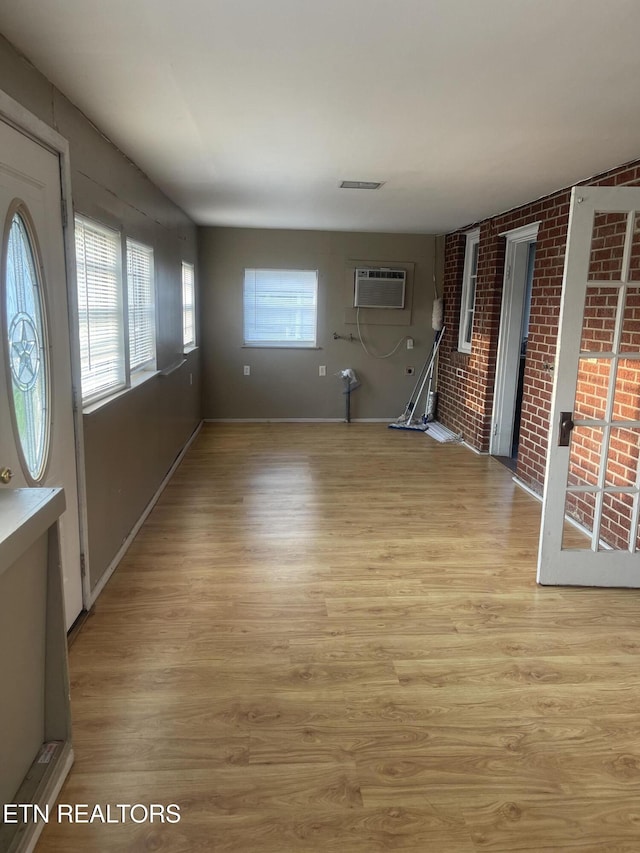 interior space with brick wall, a wall mounted AC, light wood-style flooring, and visible vents