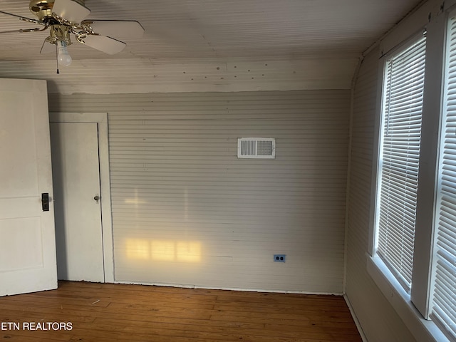 spare room with visible vents, a ceiling fan, wood walls, and hardwood / wood-style floors