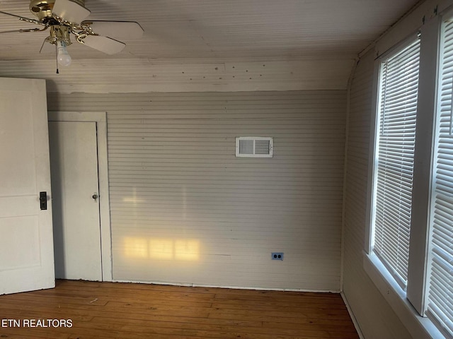 spare room featuring wooden walls, ceiling fan, hardwood / wood-style flooring, and visible vents