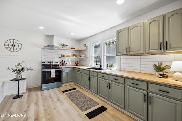 kitchen featuring a sink, wall chimney exhaust hood, green cabinets, electric stove, and backsplash