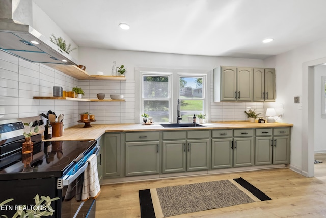 kitchen with a sink, exhaust hood, butcher block counters, decorative backsplash, and electric stove