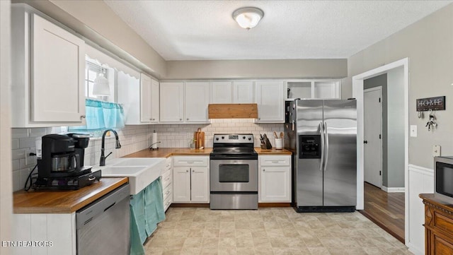 kitchen with appliances with stainless steel finishes, a sink, wood counters, white cabinetry, and backsplash