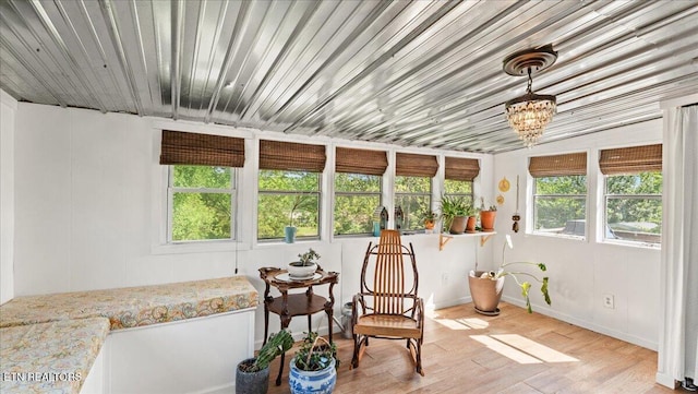 sunroom with baseboards, a notable chandelier, wood finished floors, and a wealth of natural light