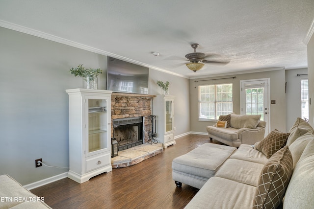 living room with ceiling fan, a stone fireplace, baseboards, dark wood-type flooring, and ornamental molding