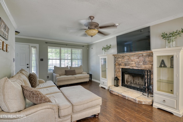 living room with crown molding, dark wood-style flooring, a stone fireplace, a ceiling fan, and baseboards