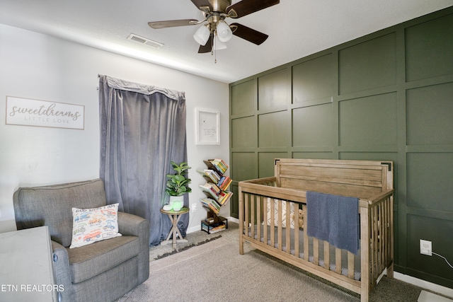 bedroom with visible vents, carpet flooring, a crib, and ceiling fan