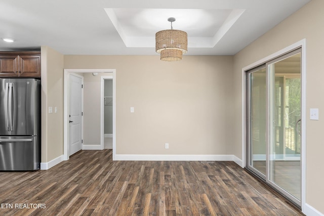 unfurnished dining area featuring an inviting chandelier, baseboards, a tray ceiling, and dark wood-type flooring