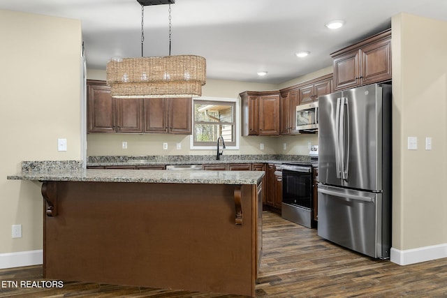 kitchen featuring appliances with stainless steel finishes, light stone counters, dark wood finished floors, a peninsula, and baseboards