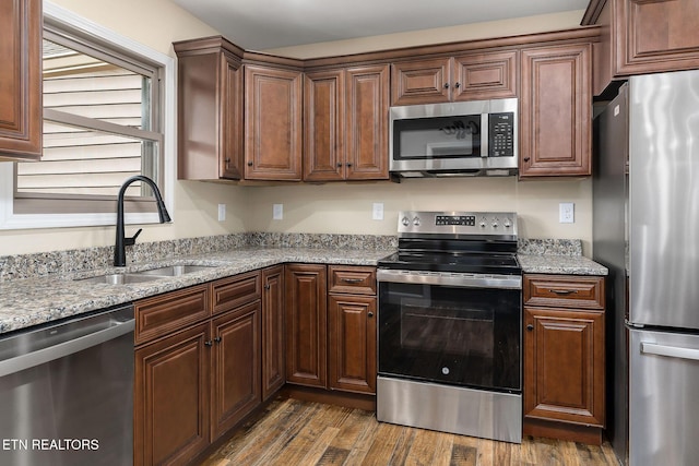 kitchen featuring dark wood-style flooring, appliances with stainless steel finishes, a sink, and light stone counters