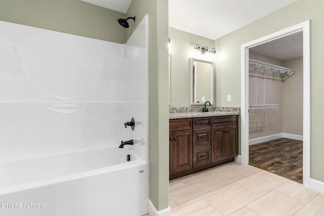 bathroom with a walk in closet, vanity, baseboards, wood finished floors, and shower / bathing tub combination