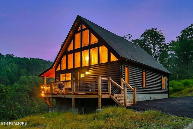 back of property at dusk featuring log exterior, a wooden deck, and roof with shingles